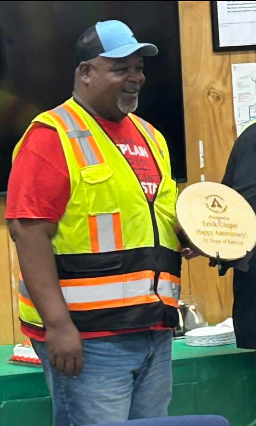 Image of Erick Coooper holding a plaque commemorating 35 years of service to the company. Erick is wearing a blue baseball cap and a bright yellow safety vest. He has a red t-shirt on underneath the vest.